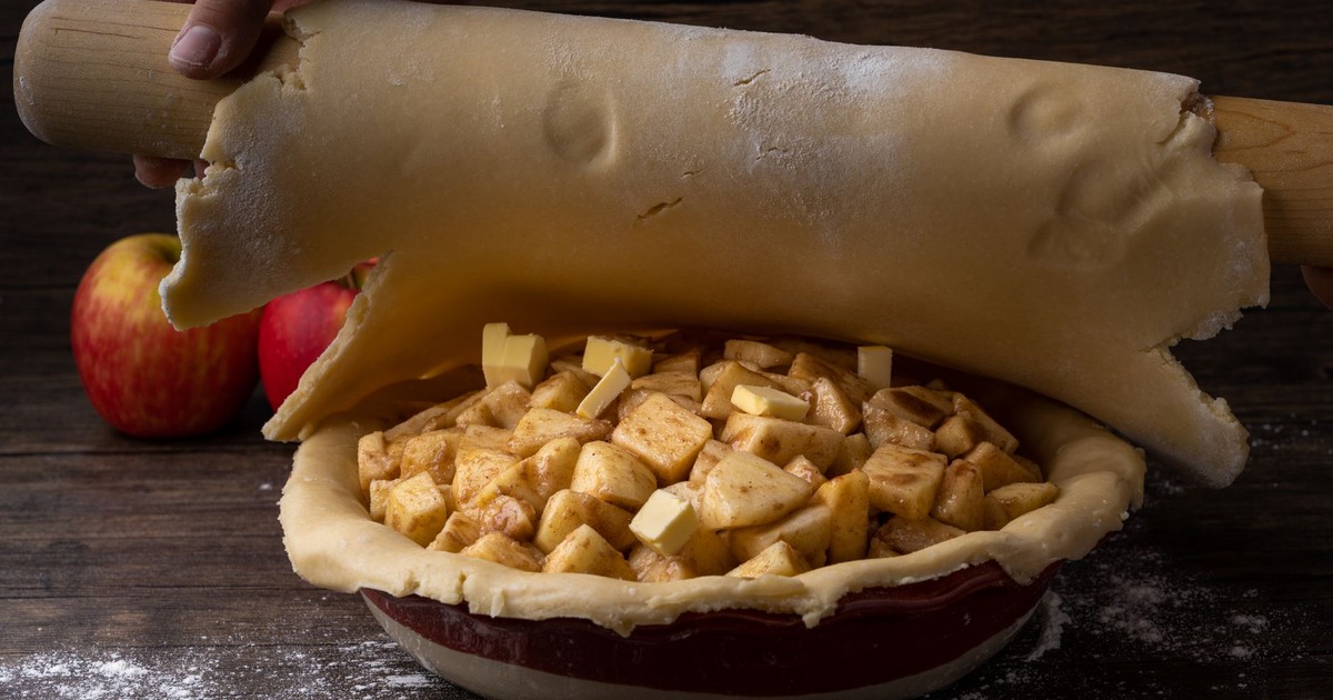 Rolling out dough for homemade apple pie with fresh apple chunks and buttery crust.