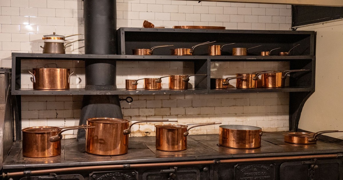 A collection of copper cookware on an old-fashioned stove in a classic kitchen setting.