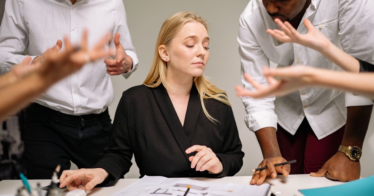 Team of professionals in a tense office discussion around a desk with documents.