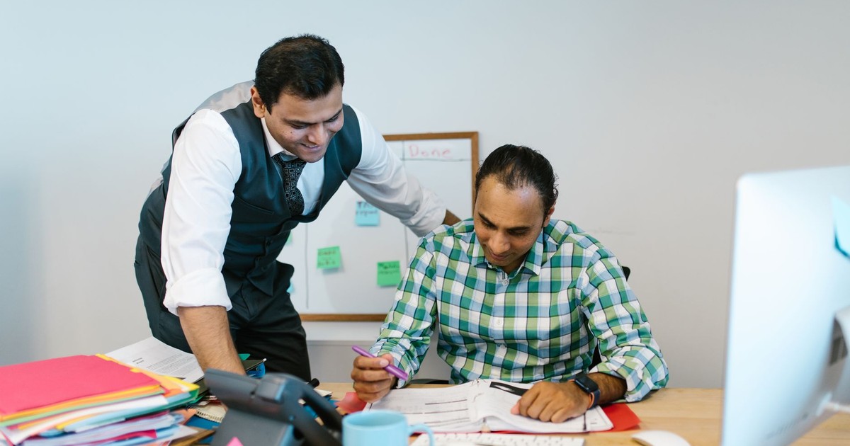 Two professional men collaborating in an office environment, reviewing documents and discussing strategies.