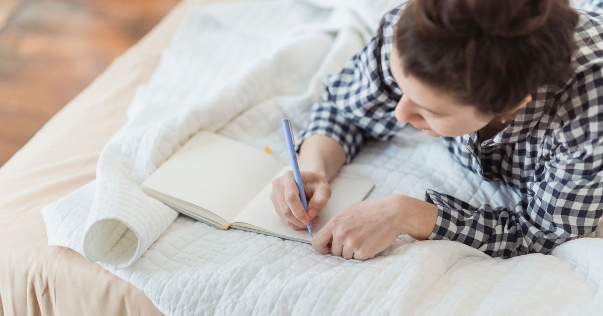 A woman writes in a journal while relaxing on a cozy bed with soft lighting and peaceful surroundings.