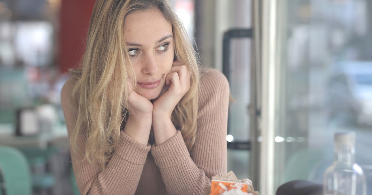 A woman in a cafe looking contemplative with a coffee cup nearby, captured with Canon EOS 5DS.
