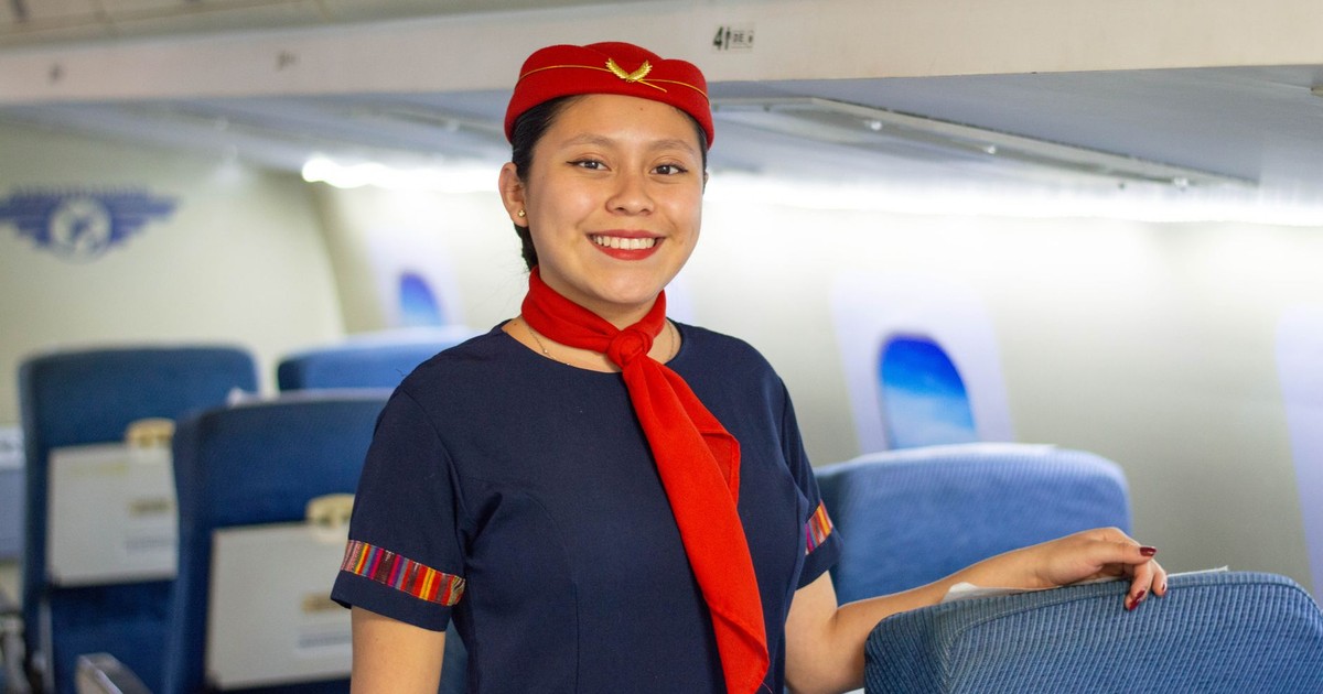Enthusiastic flight attendant wearing a red uniform stands smiling in an airplane cabin.