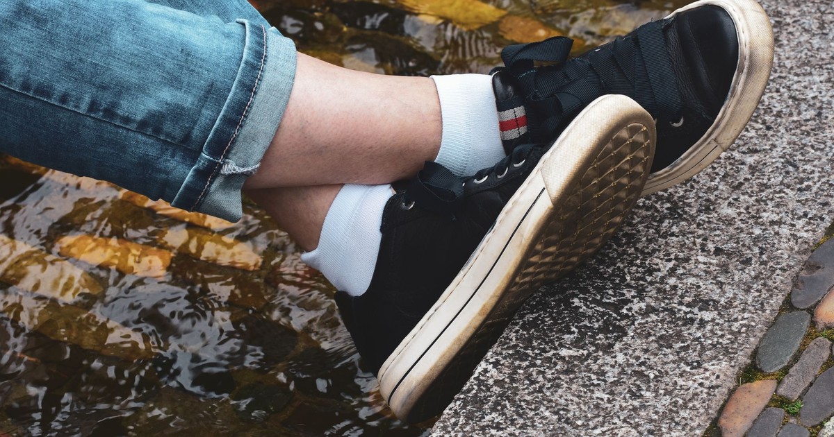 Close-up of casual sneakers on a cobblestone edge by water, capturing a relaxed outdoor moment.