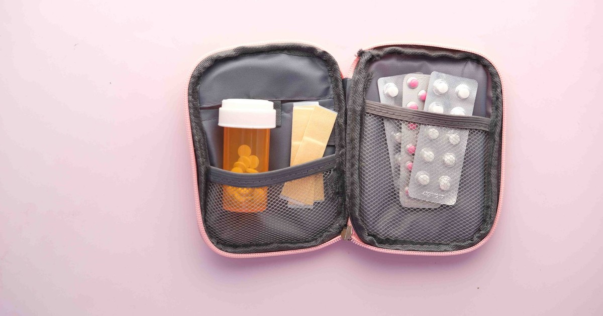 Open first aid kit with pill bottle, blister packs, and band-aids on a pastel background.
