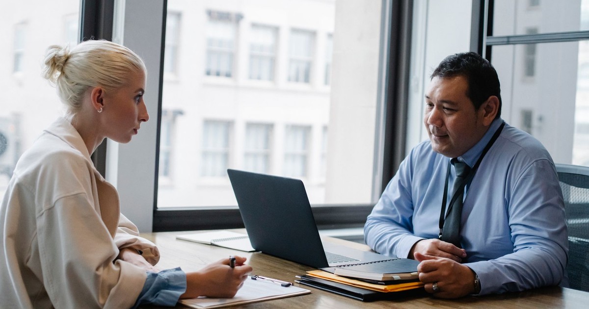 Ethnic boss asking question to female candidate filling information form on clipboard during hiring meeting