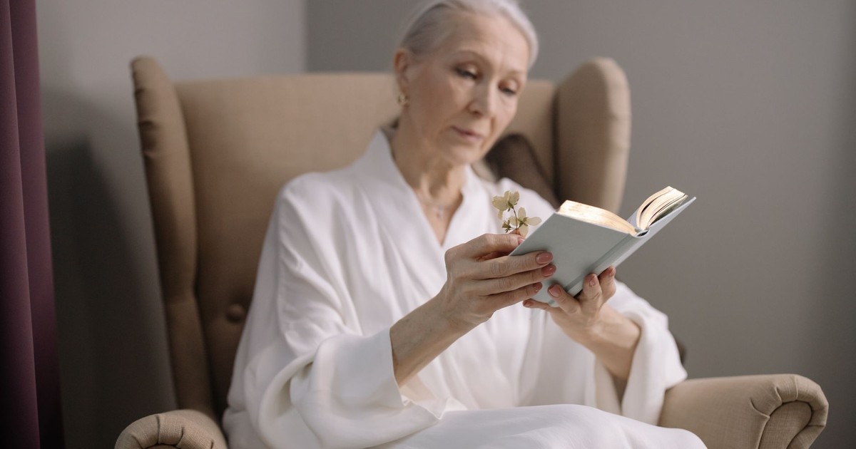 Elderly woman in an armchair reading, enjoying a peaceful indoor moment with a book.