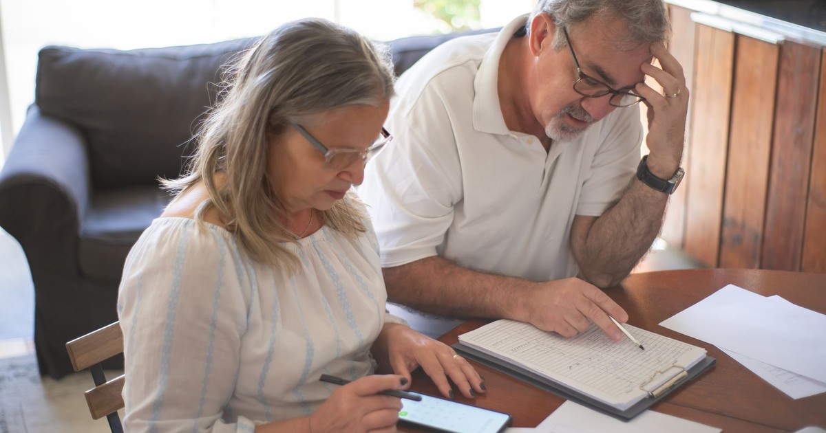 Elderly couple reviewing bills and documents at home, focusing on finances and technology.