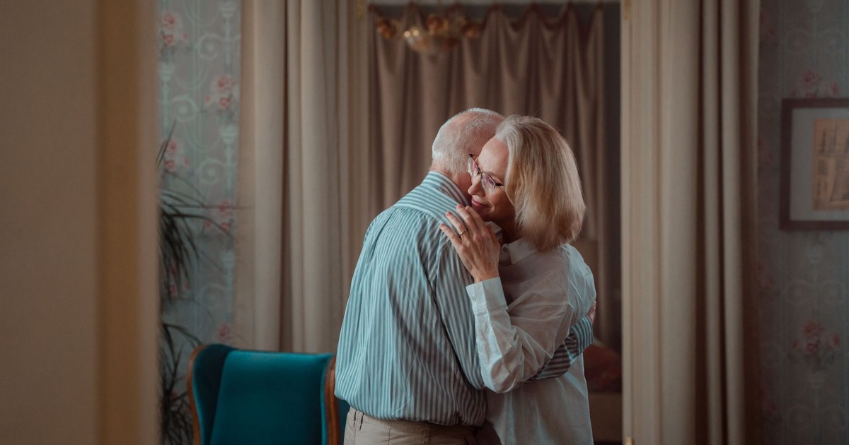 An elderly couple shares a tender embrace in a comfortable home setting, symbolizing lasting love and companionship.