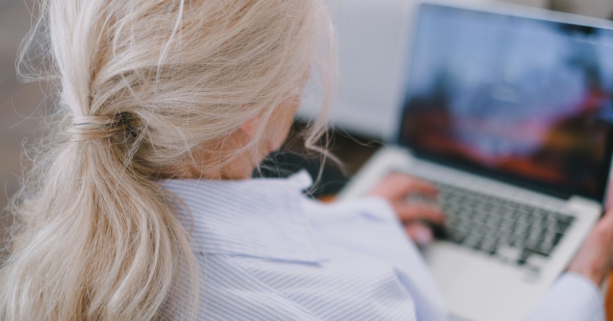 A senior woman with white hair using a laptop in a casual home setting.