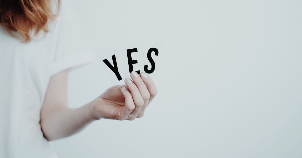 Close-up of a hand holding cards with the word 'YES' on a white background.