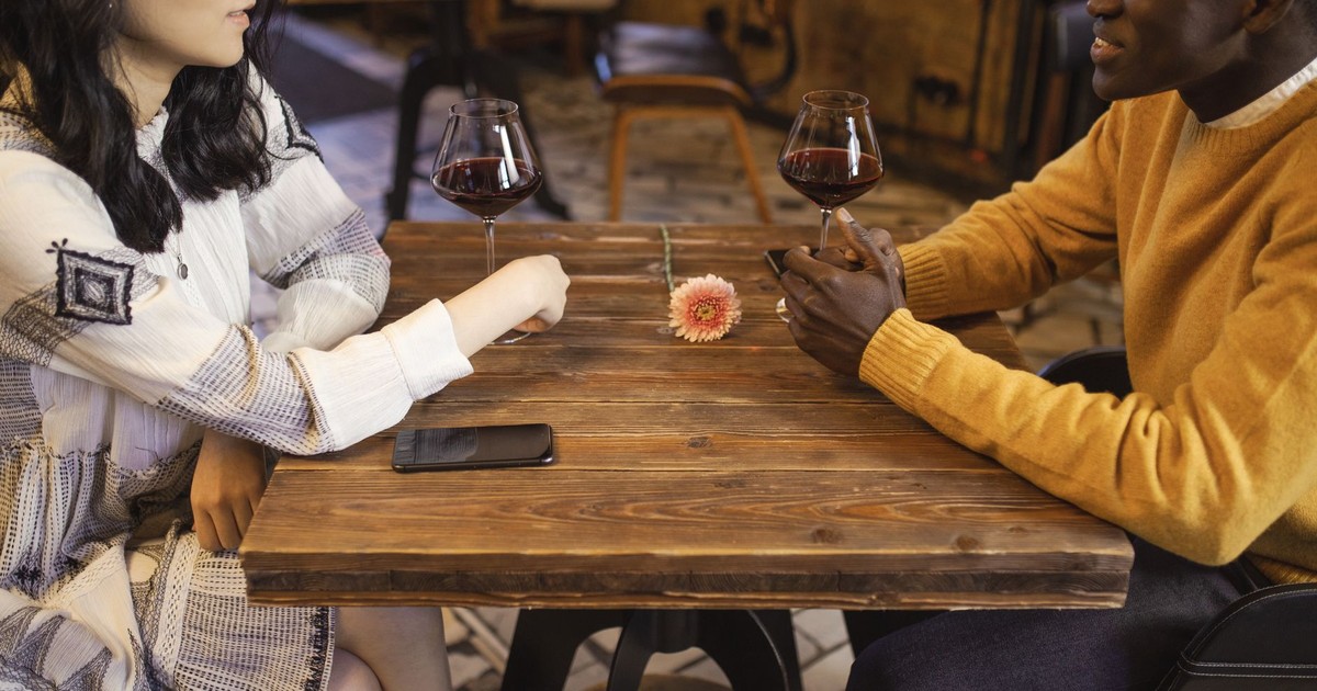 Interracial couple enjoying a romantic date with wine in a cozy café setting.