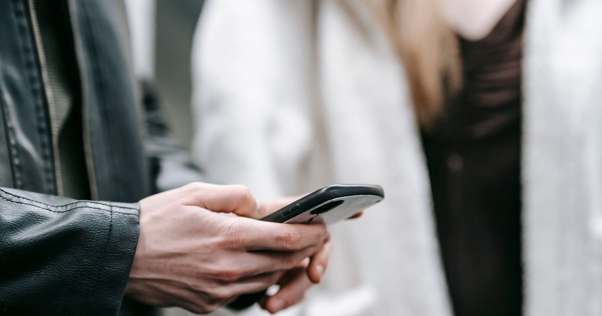 Crop faceless couple in warm clothes standing together while text messaging on phone