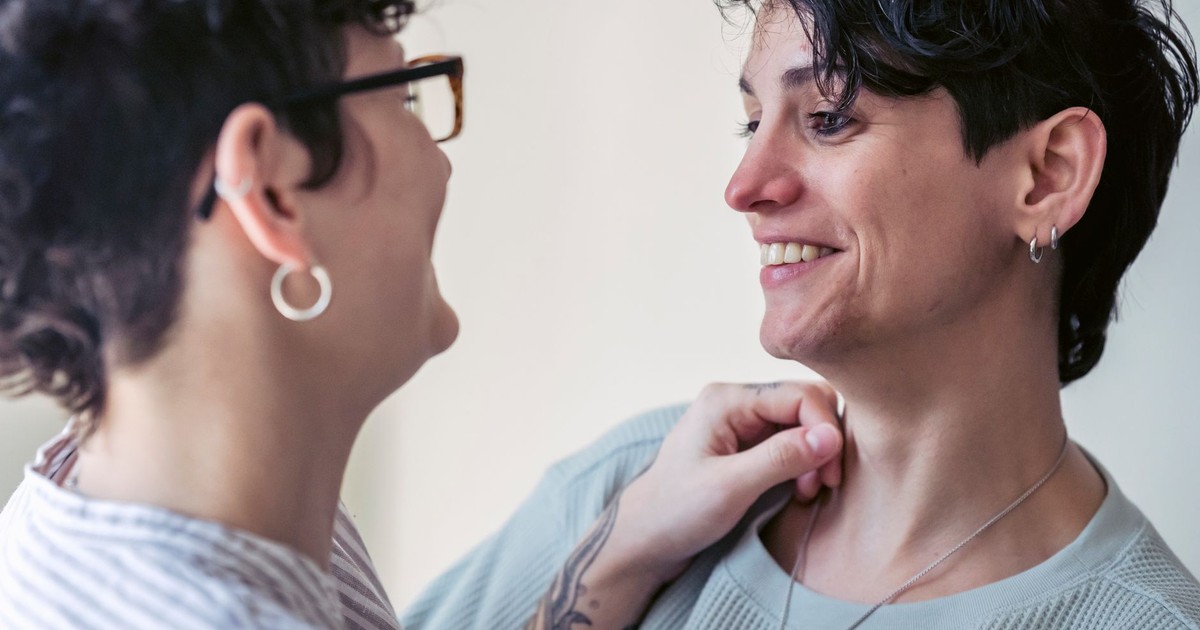 Crop cheerful tattooed woman in eyeglasses speaking with homosexual partner while looking at each other on light background