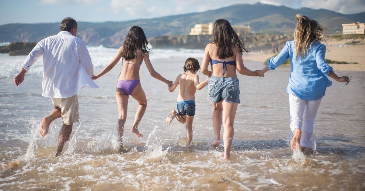 A family having fun running into the ocean on a sunny beach day in Portugal. Joyful and carefree moments.