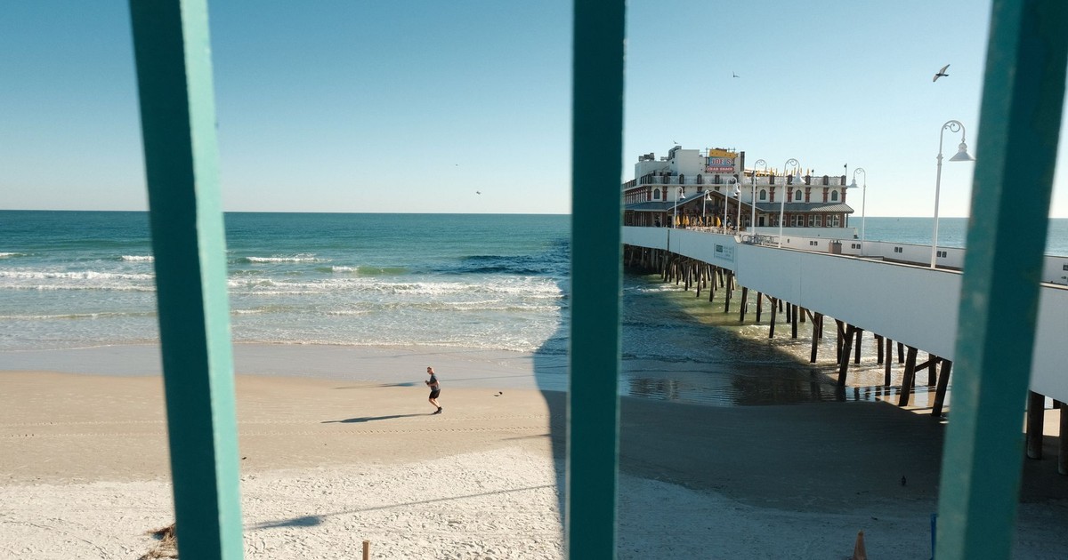A lone runner on Daytona Beach near the pier under a clear blue sky.