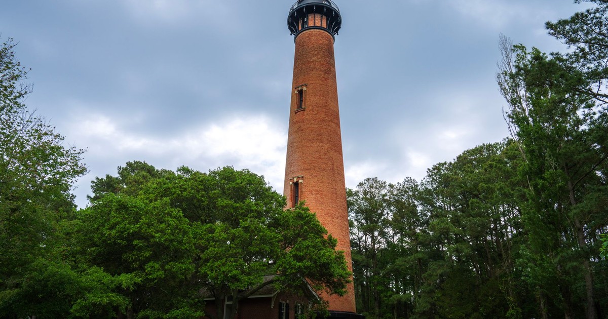 Beautiful view of Currituck Beach Lighthouse surrounded by lush trees on a cloudy day.
