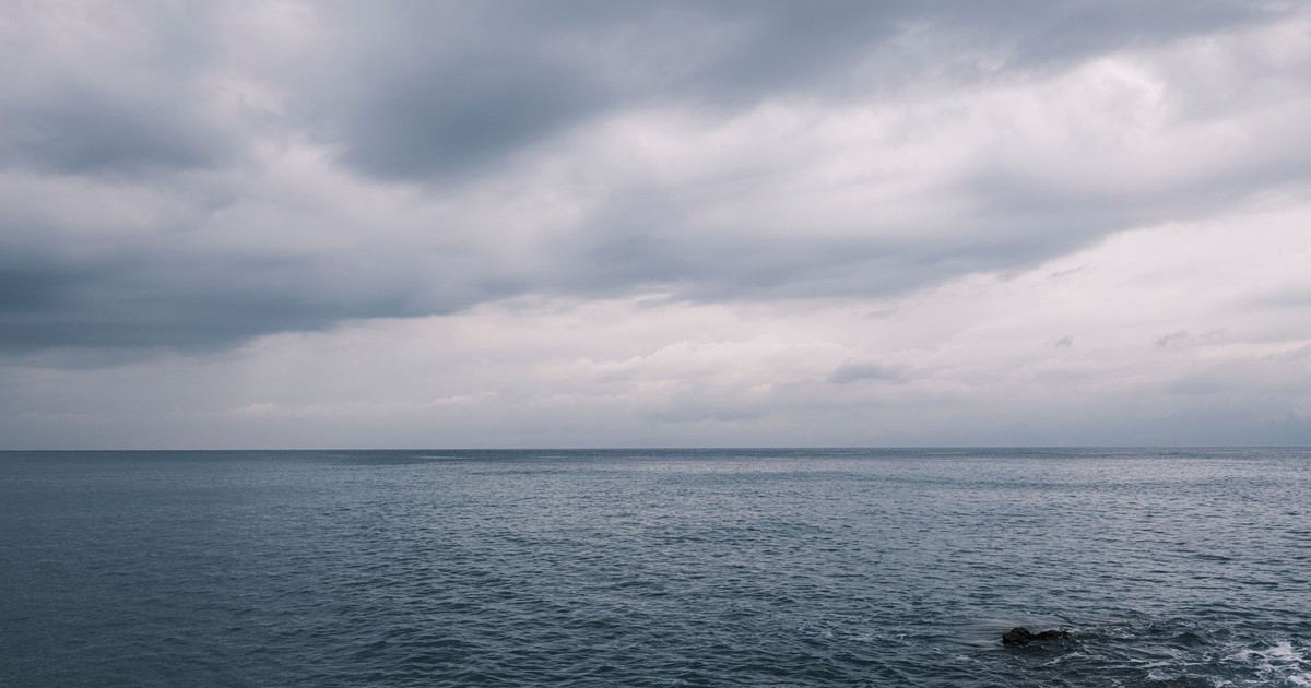 A dramatic seascape with dark clouds and turbulent waves on the horizon.