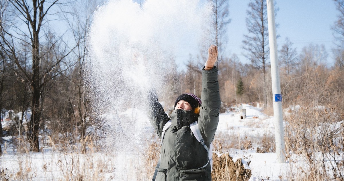 Person enjoying a sunny winter day, throwing snow in the air, surrounded by nature.