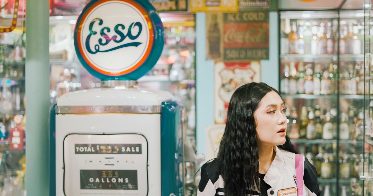 Young woman explores a vintage supermarket featuring a retro Esso gas pump and nostalgic decor.