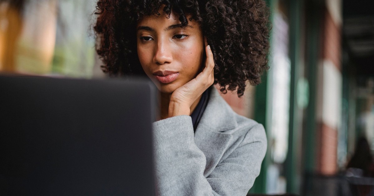 Crop attentive well dressed black female executive with Afro hairstyle touching face while watching netbook