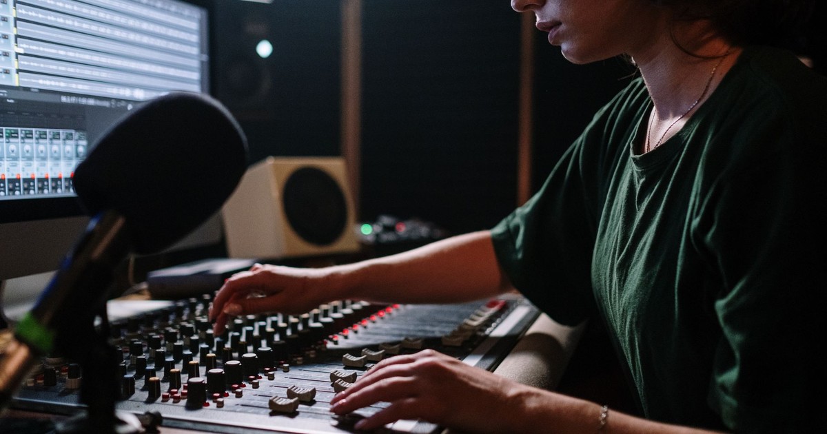 Focused woman operates a sound mixer in a music studio, enhancing audio quality.