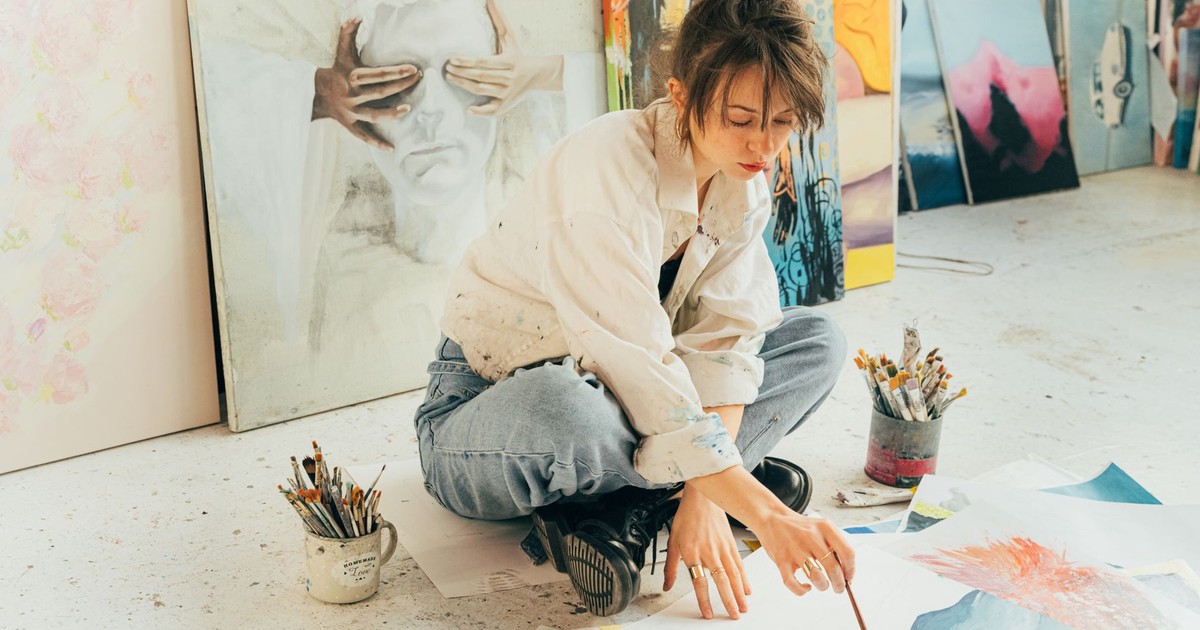 A creative young artist painting in a bright studio surrounded by artwork and brushes.