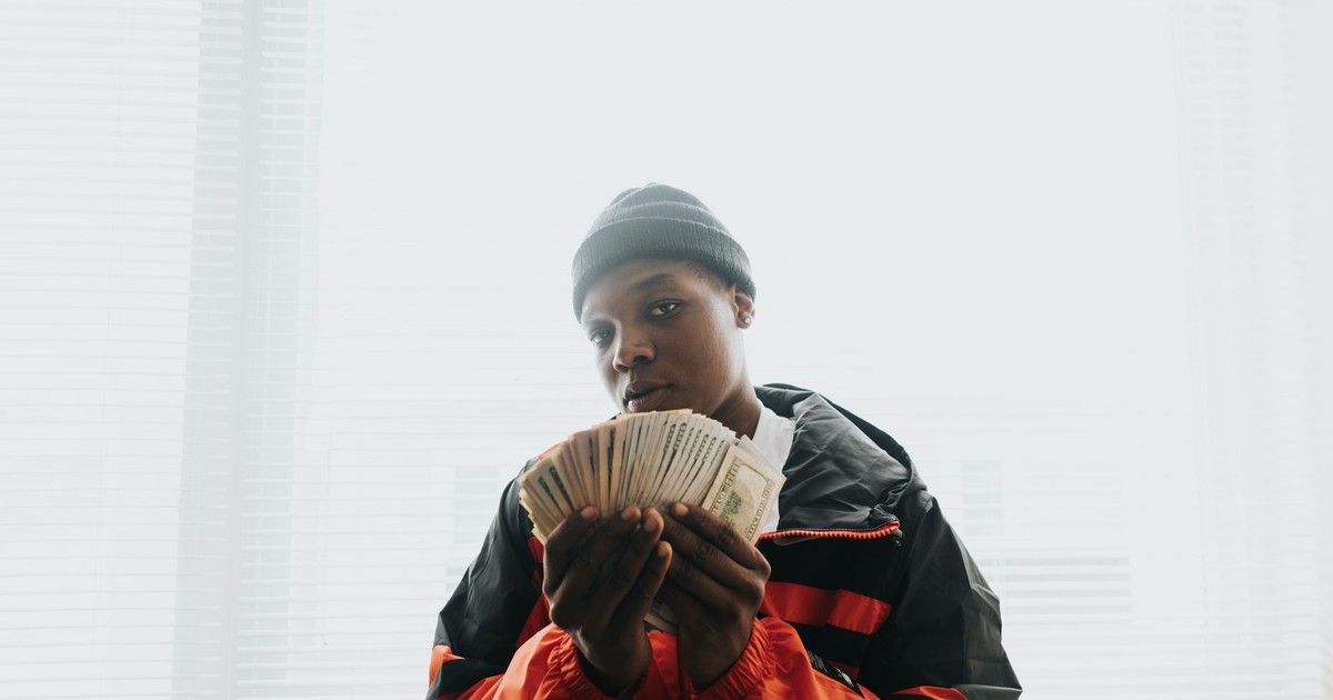 Portrait of a young man in a beanie holding a stack of dollars, indoors.