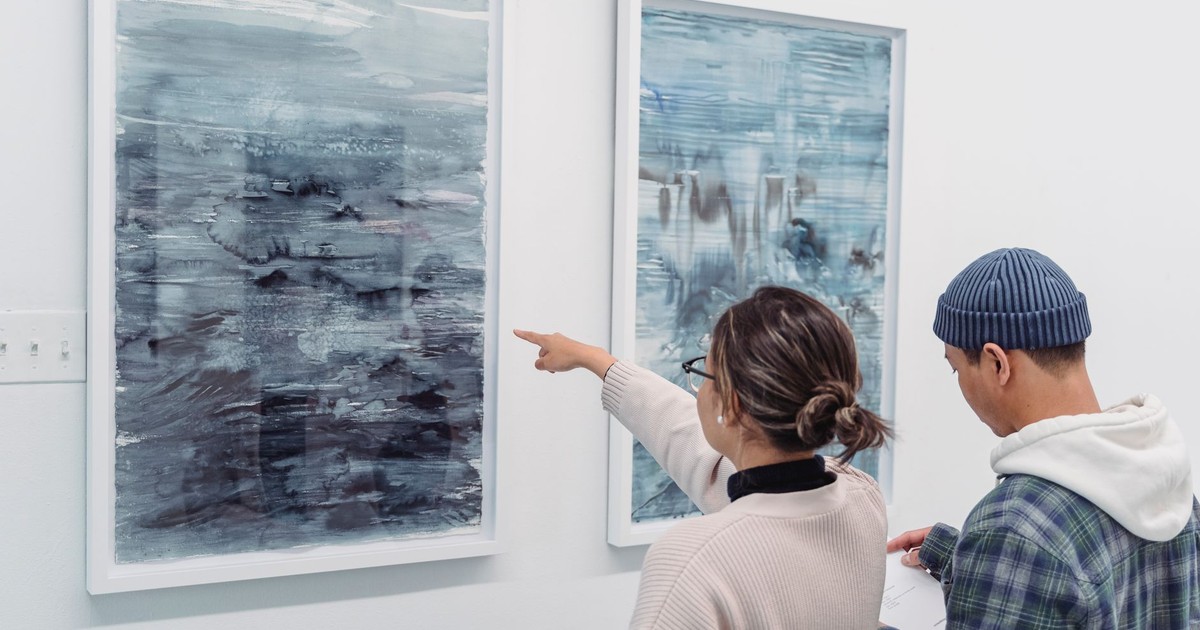 Two people examining abstract artwork in a gallery, engaging with the art.