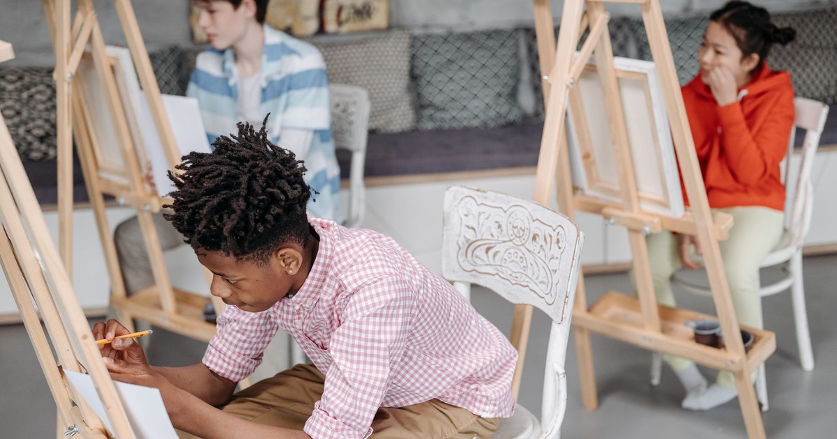 Children focused on creating art in a diverse classroom setting with easels and art materials.