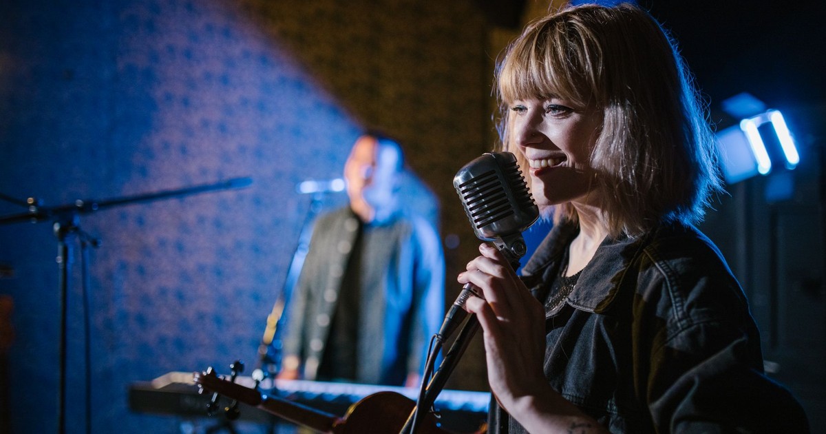 Smiling caucasian woman singing with vintage microphone during live music performance.