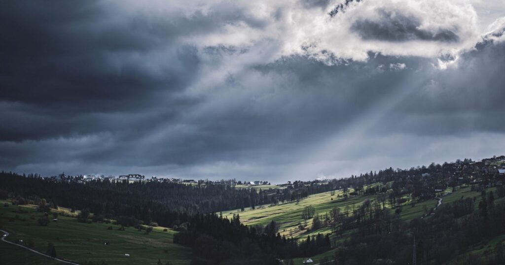 Moody landscape of Biały Dunajec, Poland, with dramatic clouds and sunlight breaking through.