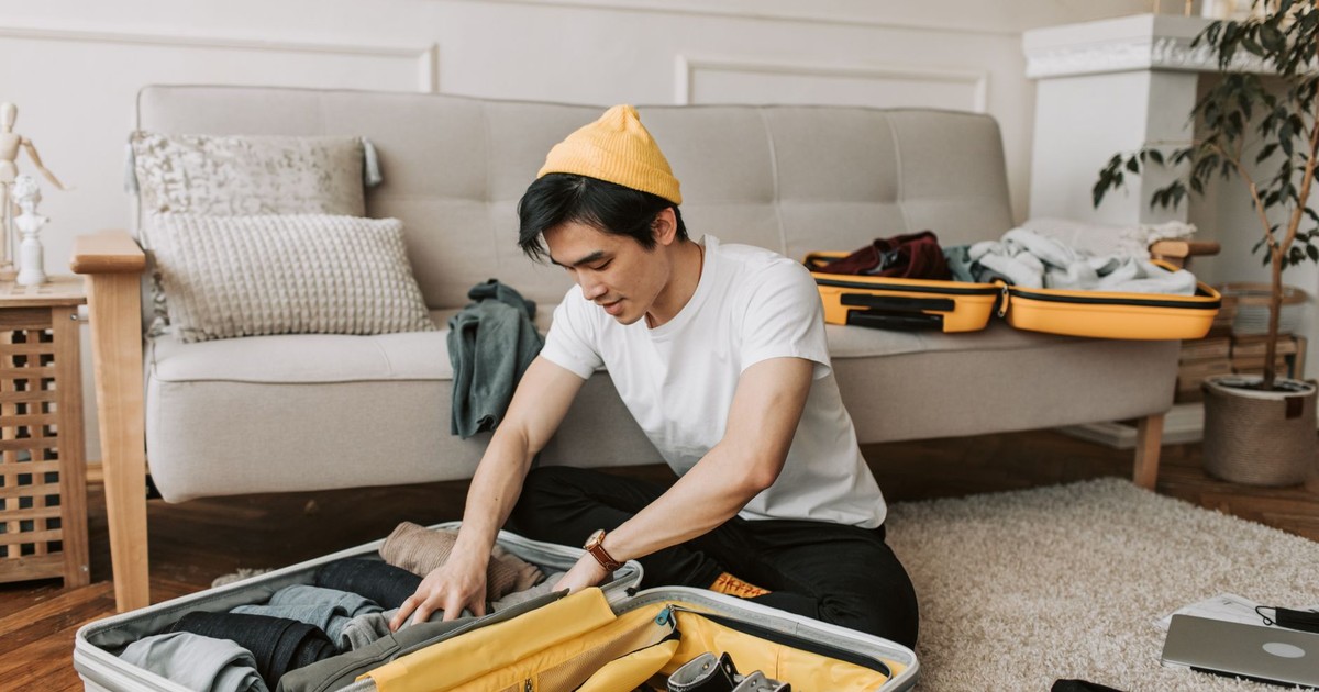 Young man organizing clothes in a suitcase in a cozy living room, preparing for travel.