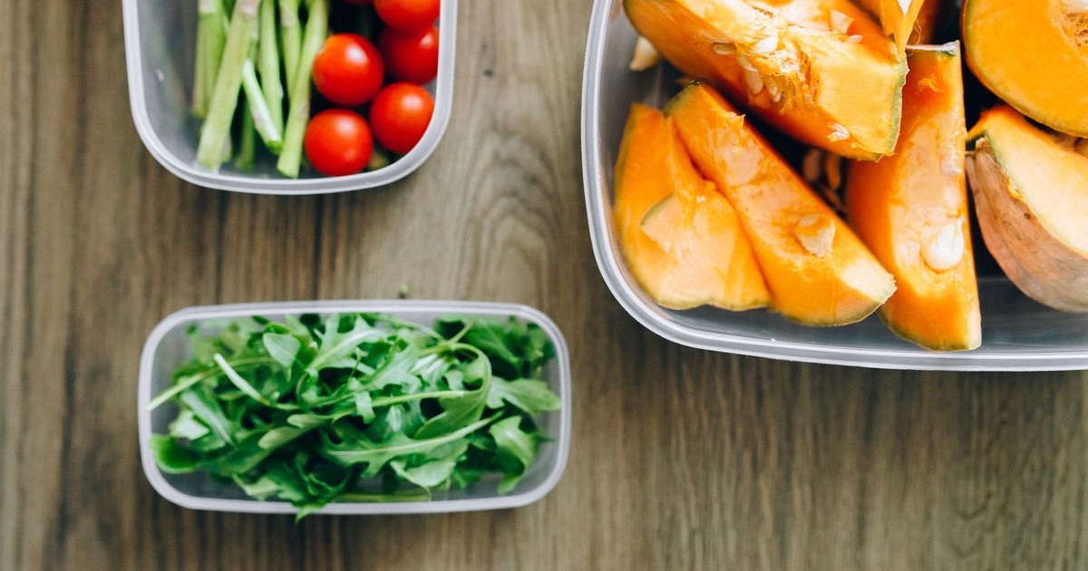 Top view of fresh ingredients including arugula, cherry tomatoes, and squash in plastic containers on wooden background.