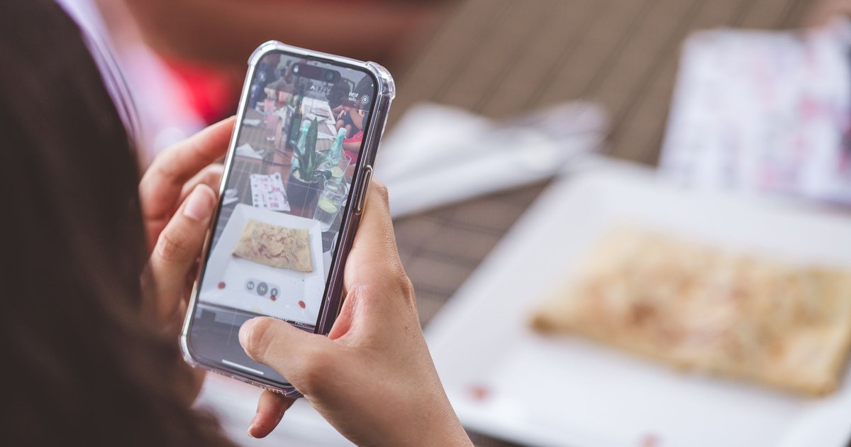Close-up of a woman photographing a meal at a restaurant using a smartphone.