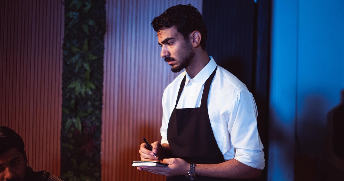 A focused waiter in uniform takes an order in a modern restaurant setting. Perfect for hospitality-themed content.