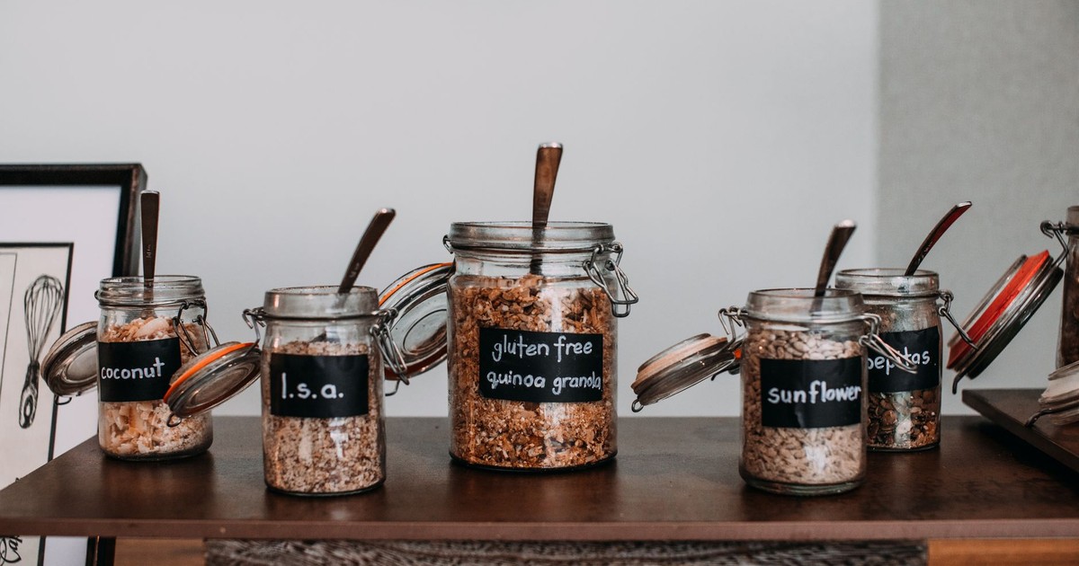 Close-up of labeled glass jars containing various grains and seeds on a wooden table.