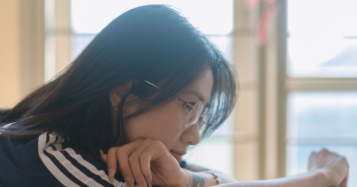 Side profile of a young woman in a relaxed, thoughtful pose by the window.