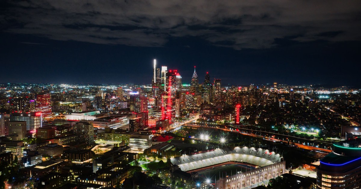 A breathtaking aerial view of Philadelphia's illuminated skyline at night, highlighting the vibrant cityscape and a prominent stadium.