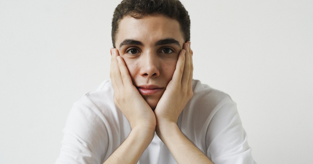 Portrait of a young man with hands on cheeks, wearing a white t-shirt.