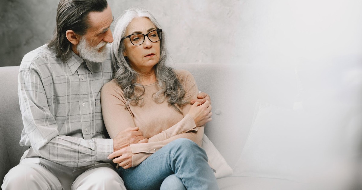 Elderly couple sitting closely, expressing comfort and support in a cozy living room setting.
