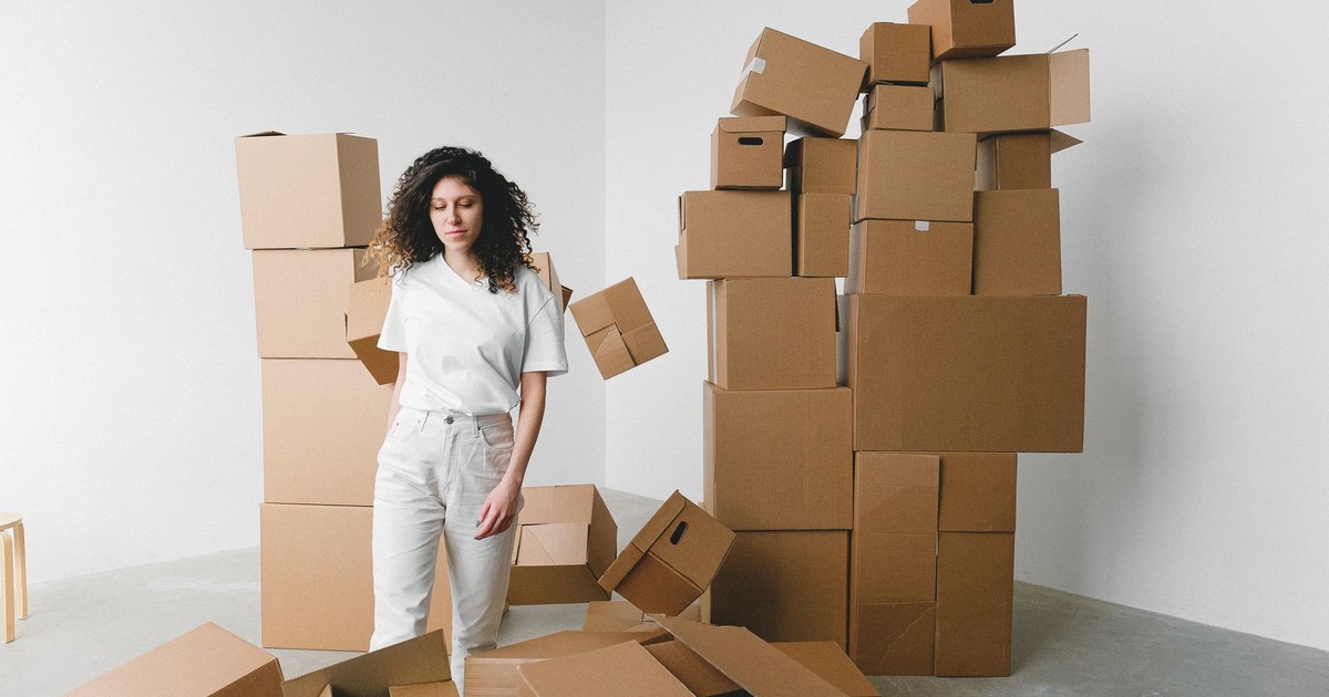 Young female with curly hair between piles and flying cardboard containers after moving into house on light background