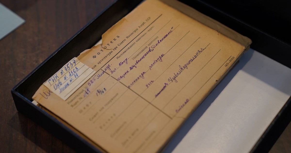 An old Russian document placed inside an archive box on a wooden desk.
