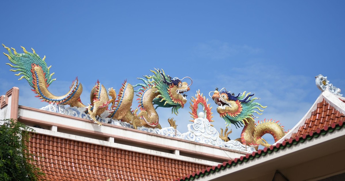 Colorful dragon sculptures adorn the roof of a Thai temple under a clear blue sky.