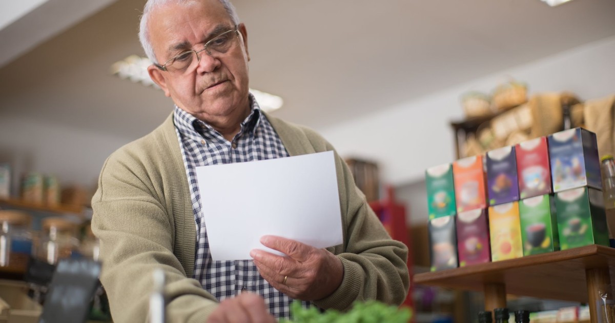 Elderly man shopping in a Portuguese grocery store, holding a paper list.