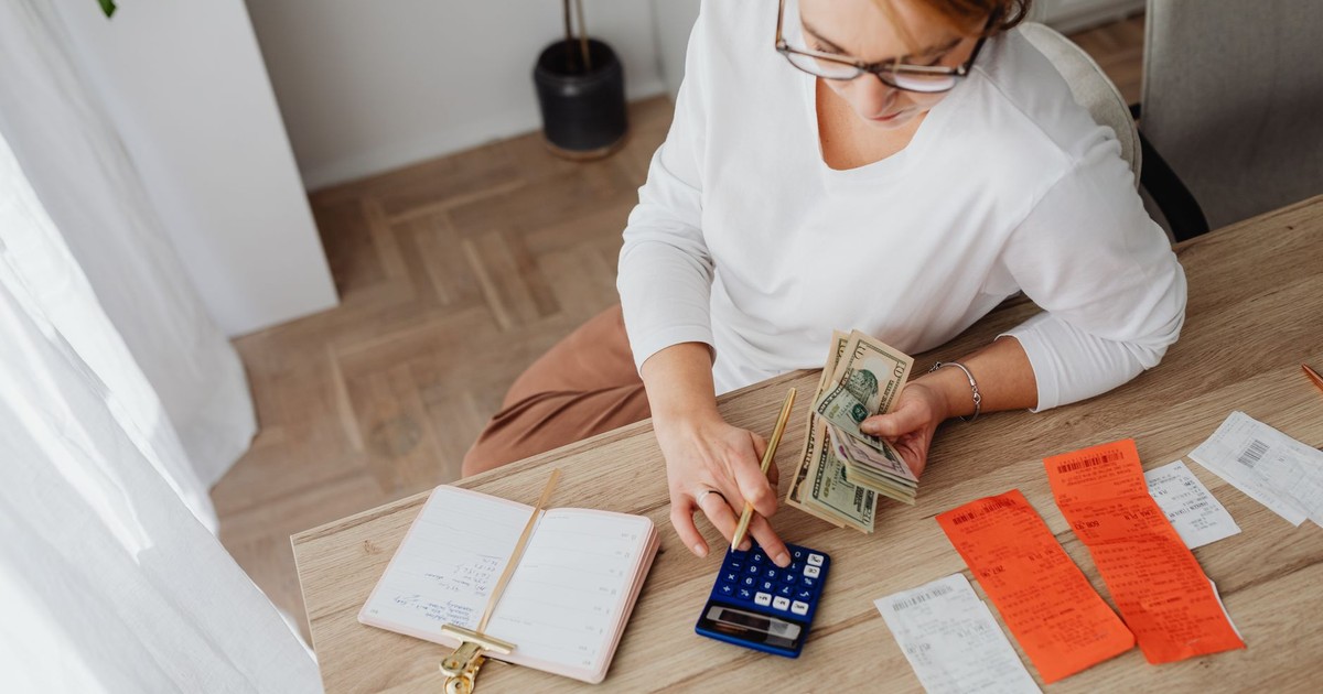 Top view of a woman managing finances with a calculator, cash, and bills in a home setting.