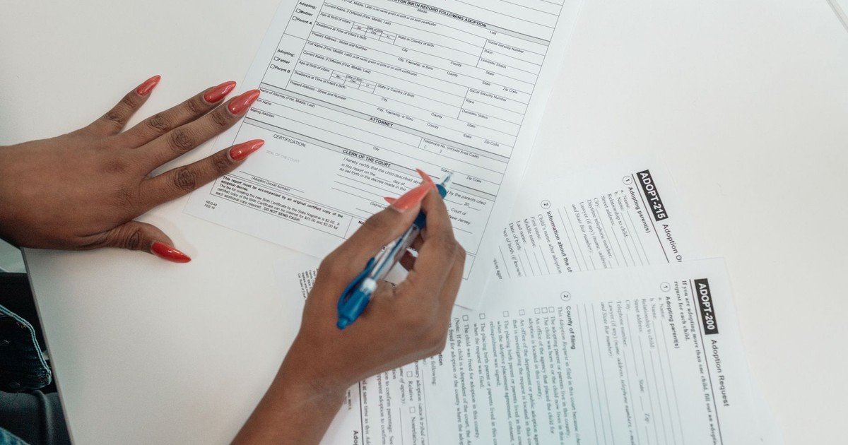 A woman with red nails fills out adoption application forms on a desk.