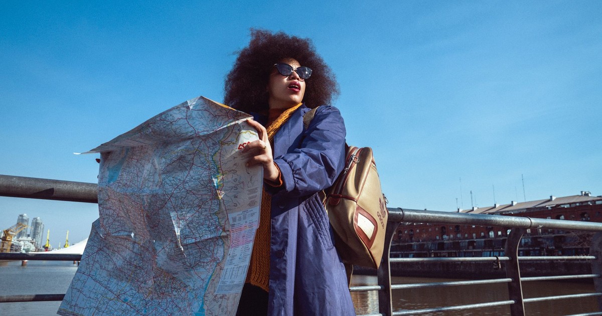 African American woman holds a map on a sunny day by the river, showcasing her adventurous spirit.