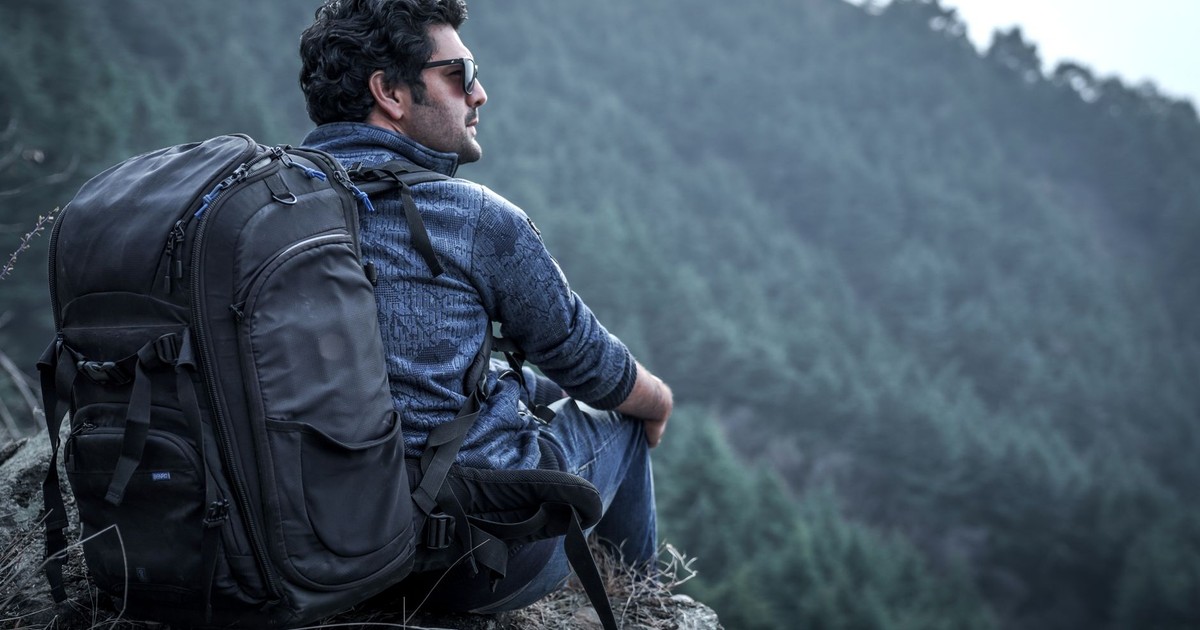 Backpacker sitting on cliff edge in forested mountains looking relaxed and adventurous.