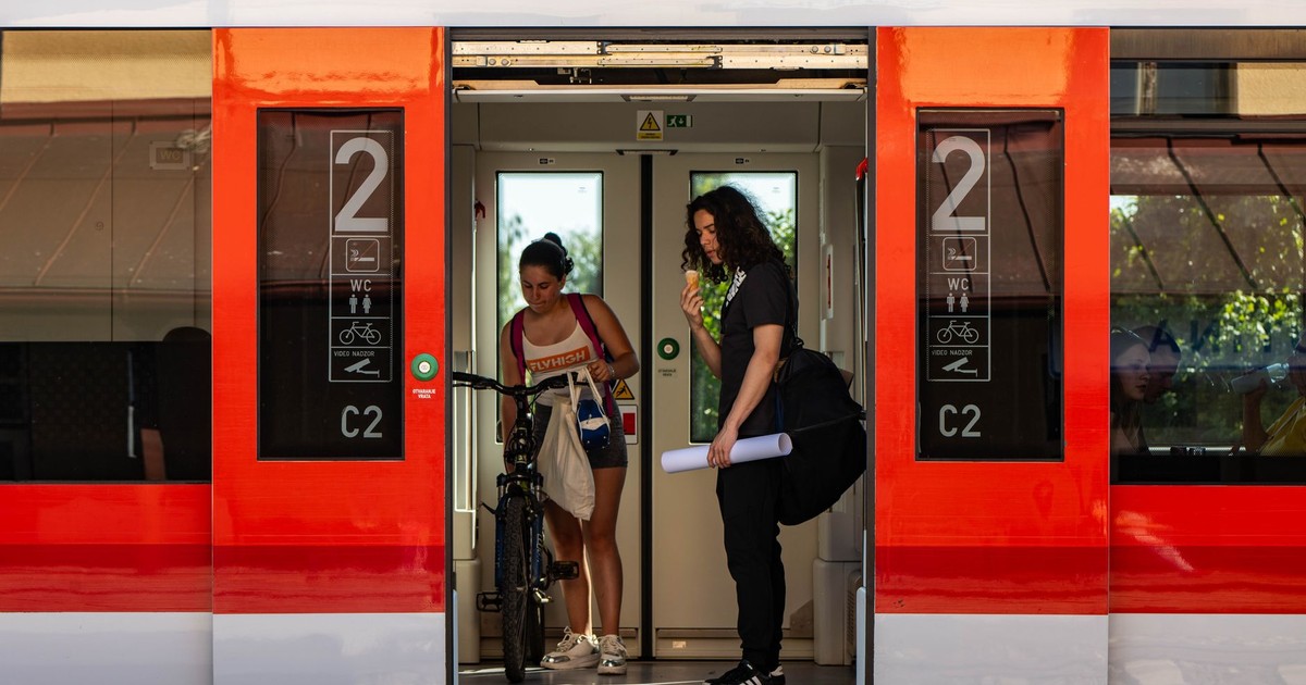 Two people with a bicycle stand at a train door, one eating ice cream.